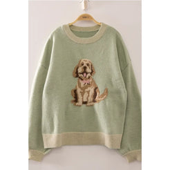 A sage green knit sweater hanging on a wooden hanger, featuring a knitted dog graphic on the chest with beige and brown tones and a small pink bow accent.
