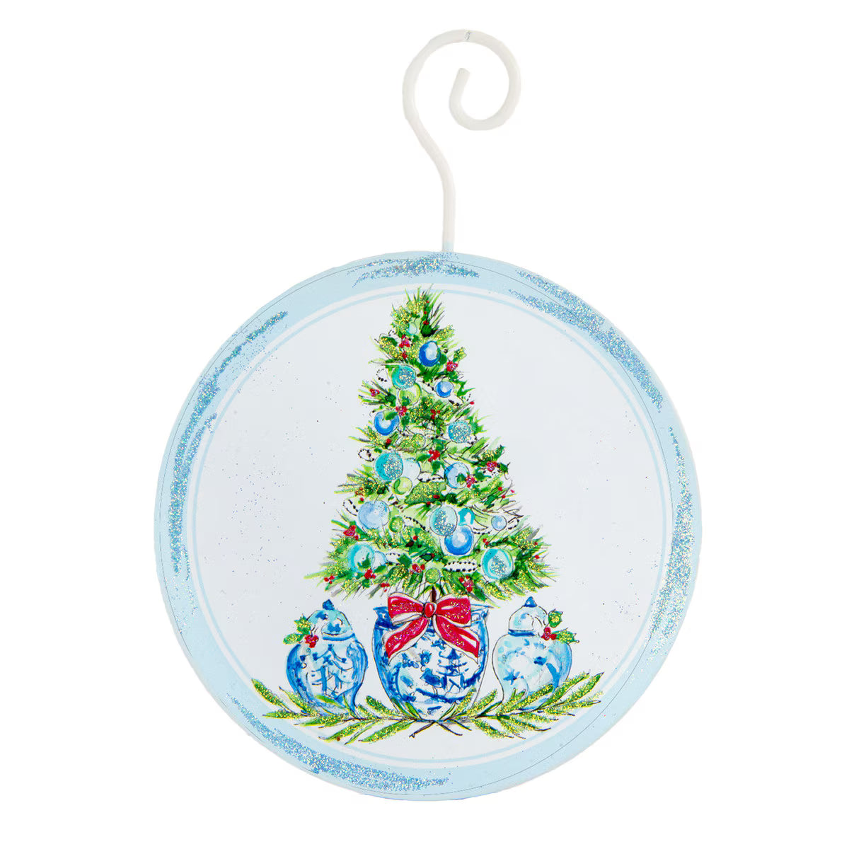Round hanging ornament with a distressed light blue border and a painted Christmas tree in the center, decorated with blue ornaments, green pine branches, and three blue-and-white gingerbread houses under a red bow, shown on a white background.