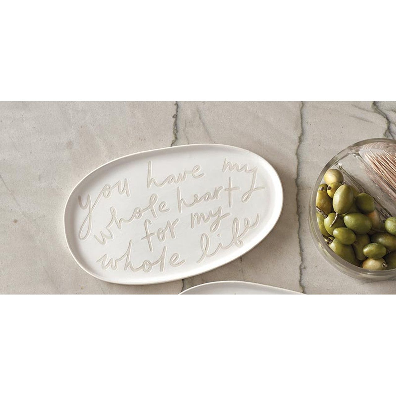 Three ceramic plates with scripted text on a marble surface with a bowl of olives.