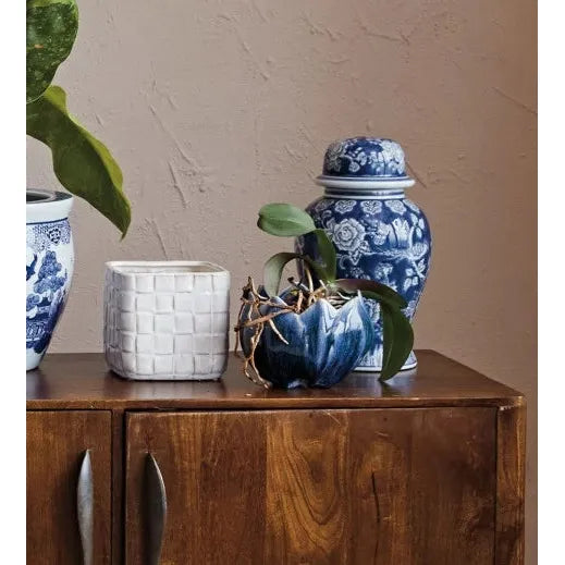 Wooden cabinet with decorative vases, books, and plants against a beige wall.
