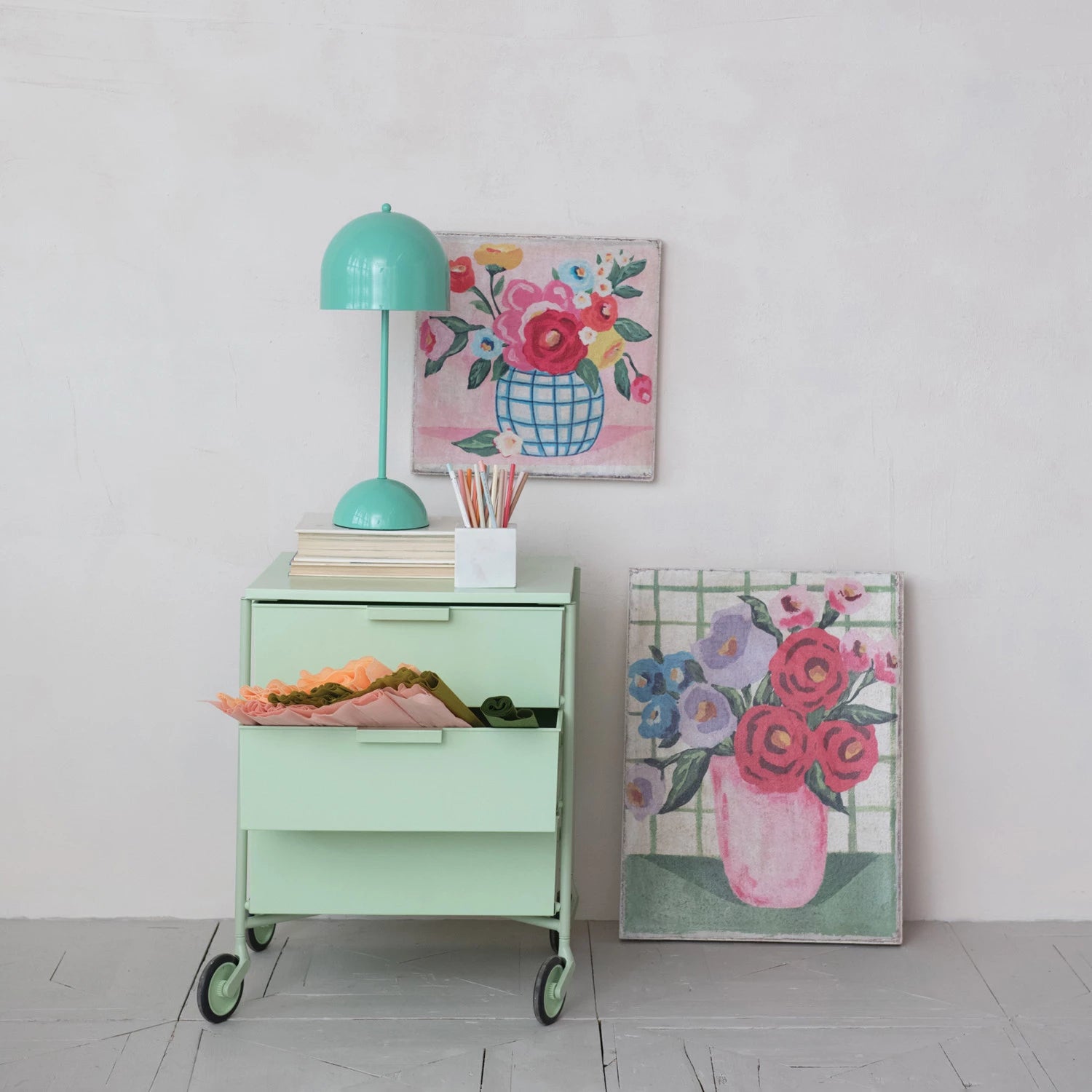 Green side table with lamp and books, floral artwork on a white wall