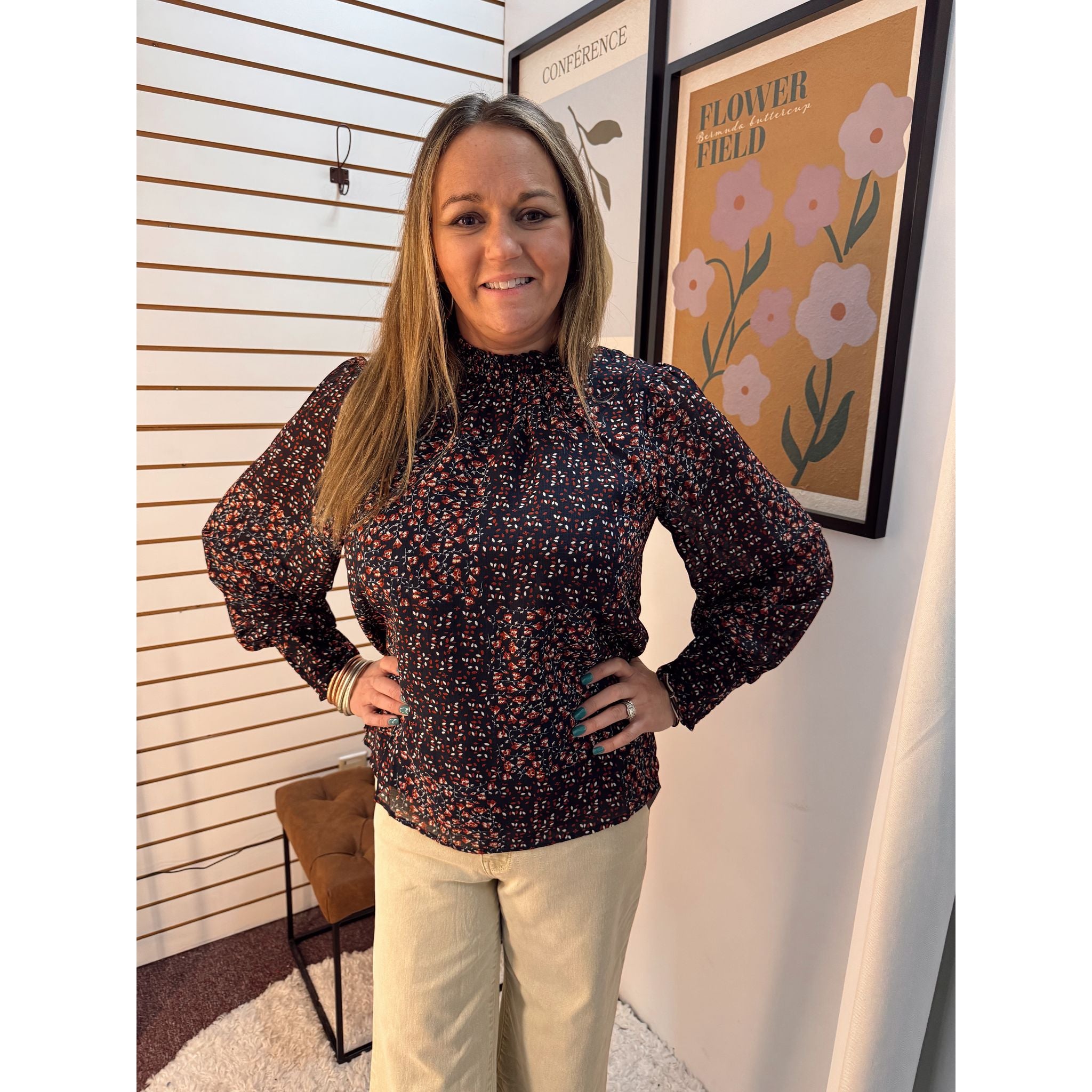 Woman wearing a patterned blouse standing in front of a wall with a floral poster.